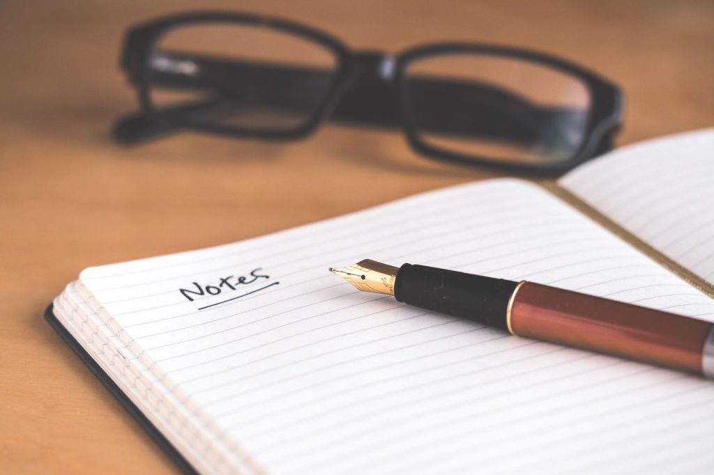 notepad with pen and glasses on table